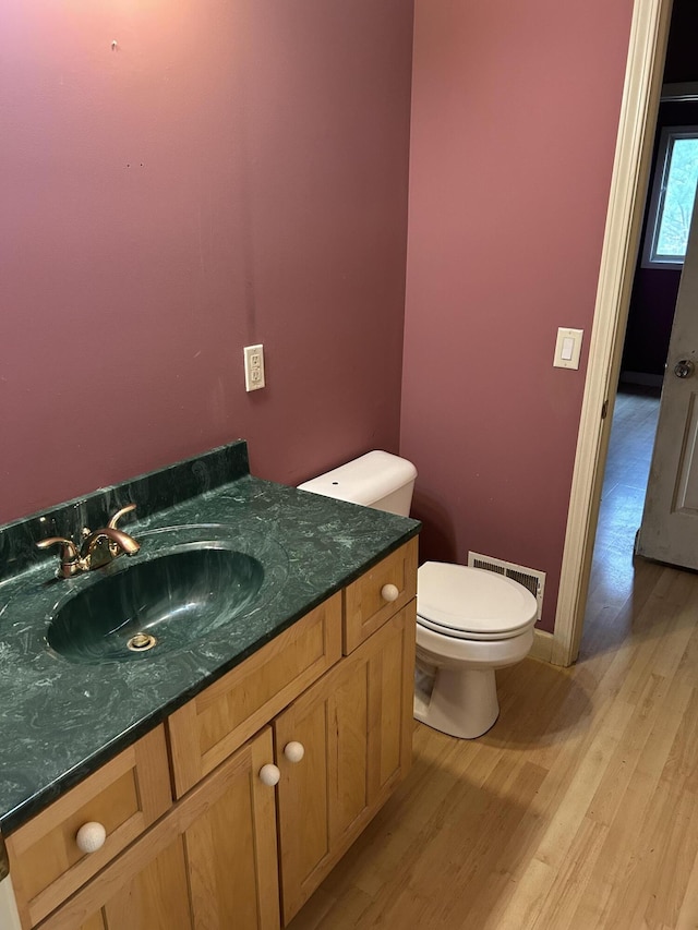 bathroom with toilet, wood finished floors, visible vents, baseboards, and vanity