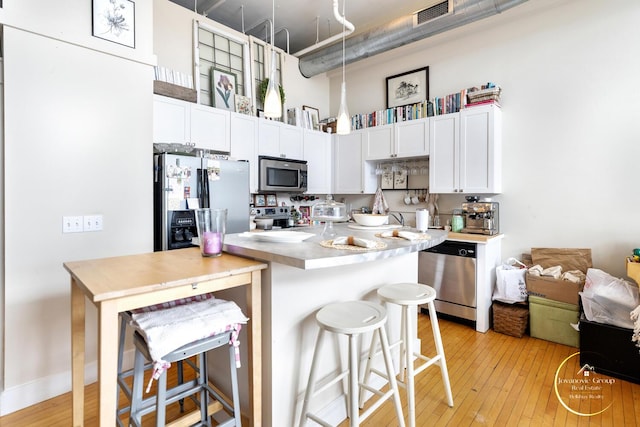 kitchen with stainless steel appliances, a kitchen breakfast bar, visible vents, light wood finished floors, and white cabinetry