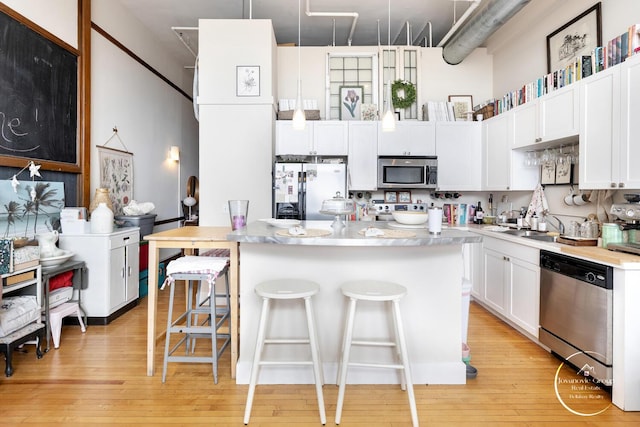 kitchen with light wood-style floors, stainless steel appliances, a kitchen breakfast bar, and white cabinetry