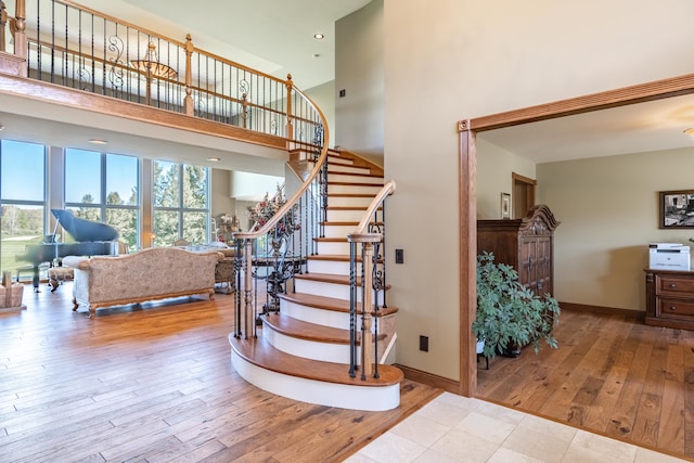 staircase featuring hardwood / wood-style floors, healthy amount of natural light, baseboards, and a towering ceiling