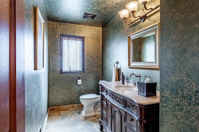 bathroom featuring vanity, toilet, baseboards, and stone finish flooring