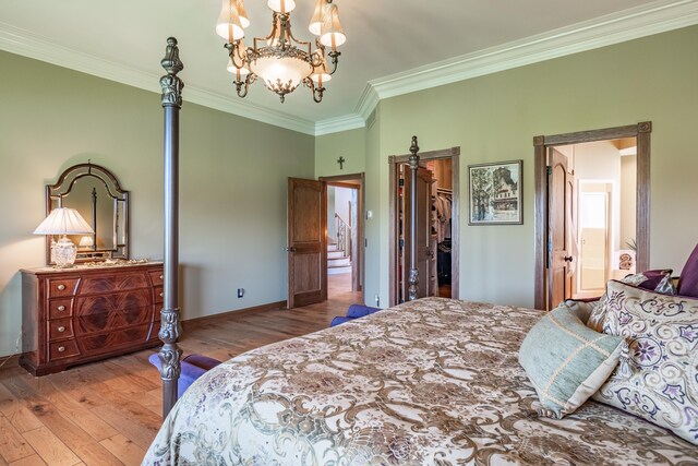 bedroom featuring ornamental molding, hardwood / wood-style floors, a chandelier, baseboards, and a spacious closet