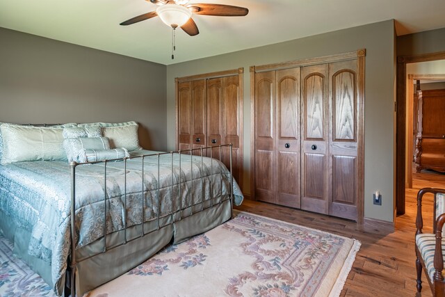 bedroom with multiple closets, wood finished floors, and ceiling fan