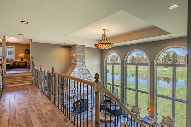 corridor with a water view, recessed lighting, hardwood / wood-style floors, and a tray ceiling