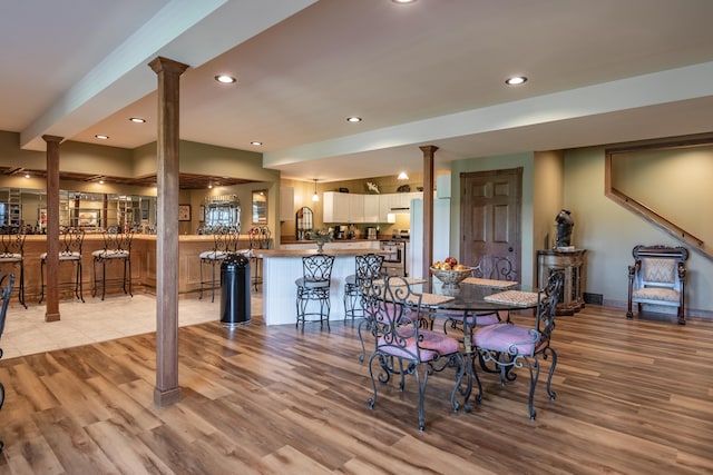 dining space featuring decorative columns, light wood-type flooring, recessed lighting, bar area, and baseboards
