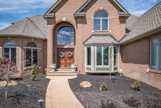doorway to property with a shingled roof and brick siding