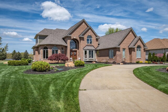 view of front of house with brick siding, a front yard, roof with shingles, and curved driveway