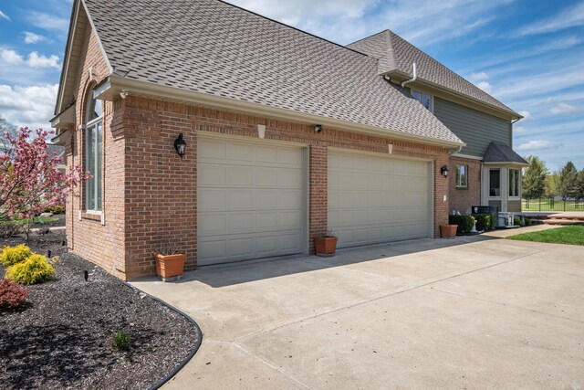 view of side of home with a shingled roof, brick siding, a garage, and concrete driveway