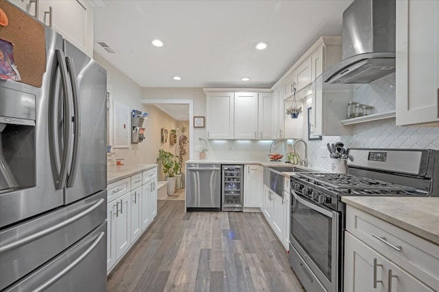 kitchen with wine cooler, recessed lighting, a sink, wall chimney range hood, and appliances with stainless steel finishes
