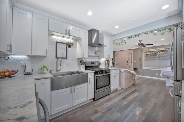 kitchen with ceiling fan, a sink, wall chimney exhaust hood, backsplash, and appliances with stainless steel finishes