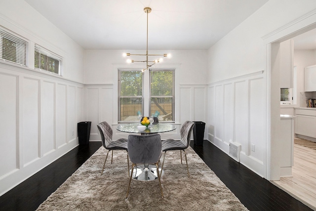 dining area featuring a wainscoted wall, an inviting chandelier, a decorative wall, and dark wood-style floors