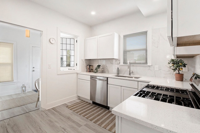 kitchen featuring a sink, a healthy amount of sunlight, light wood-type flooring, stainless steel dishwasher, and backsplash