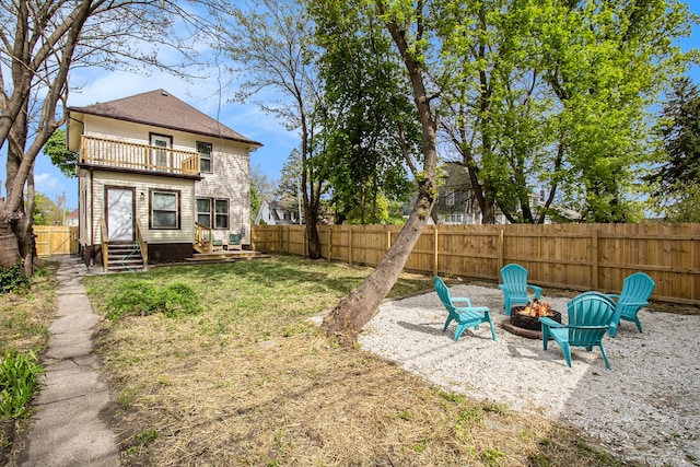 view of yard featuring an outdoor fire pit, entry steps, a fenced backyard, and a balcony