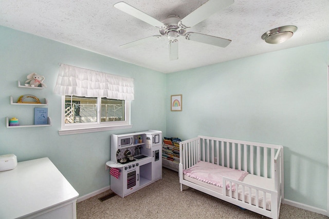 bedroom with a crib, light carpet, baseboards, a ceiling fan, and a textured ceiling