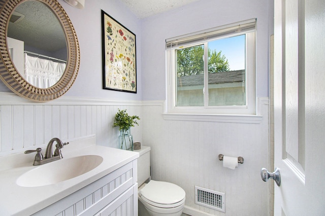 full bathroom with wainscoting, toilet, a textured ceiling, and vanity