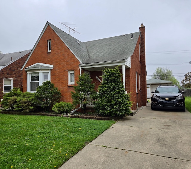 view of front of house with a chimney, brick siding, a detached garage, a shingled roof, and a front lawn