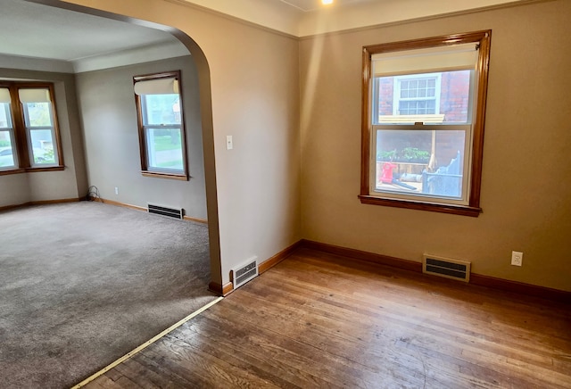 empty room with wood-type flooring, visible vents, baseboards, and arched walkways