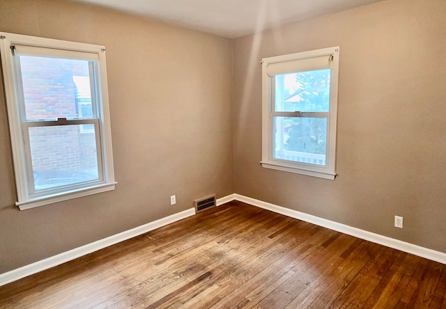 empty room with hardwood / wood-style flooring, a wealth of natural light, baseboards, and visible vents