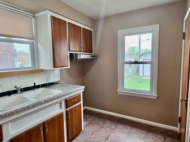 kitchen with under cabinet range hood, a wealth of natural light, baseboards, and a sink