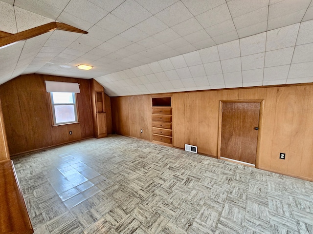 additional living space featuring baseboards, wood walls, and visible vents