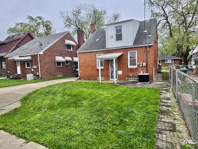 rear view of property with a yard, cooling unit, brick siding, and fence