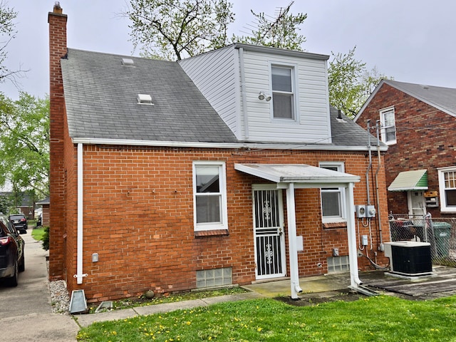 back of house featuring a chimney, central air condition unit, roof with shingles, and brick siding
