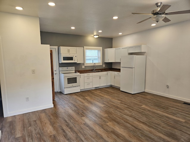 kitchen with a sink, white appliances, dark wood finished floors, white cabinets, and dark countertops