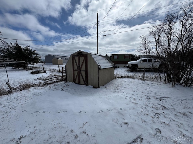 snow covered structure featuring an outdoor structure and a shed