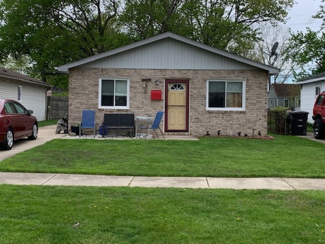bungalow-style home with brick siding, a front lawn, and fence