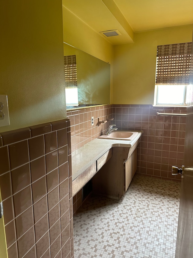bathroom featuring tile walls, vanity, visible vents, and wainscoting