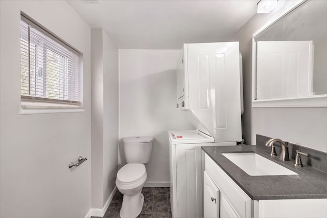 bathroom with stacked washing machine and dryer, toilet, vanity, baseboards, and tile patterned flooring