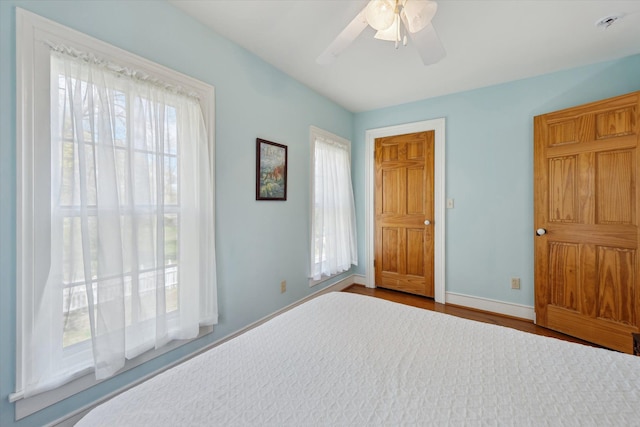 unfurnished bedroom featuring multiple windows, baseboards, wood finished floors, and ceiling fan