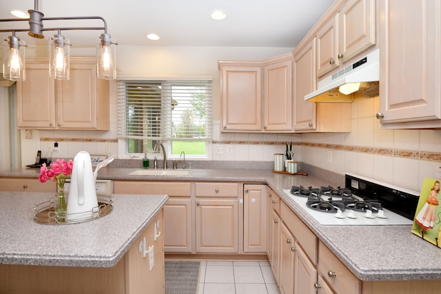 kitchen with under cabinet range hood, light tile patterned floors, a sink, stovetop, and backsplash