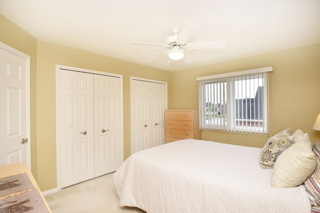 bedroom featuring a ceiling fan, light carpet, multiple closets, and baseboards