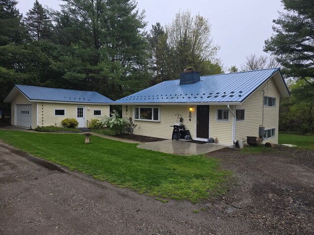 view of front facade with a front yard, a chimney, driveway, metal roof, and a garage