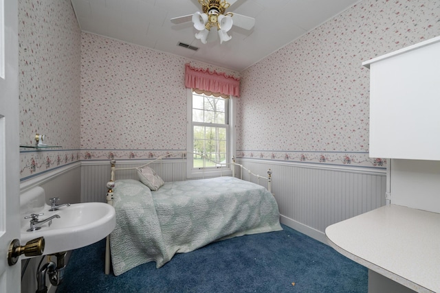 carpeted bedroom featuring ceiling fan, visible vents, wainscoting, and wallpapered walls