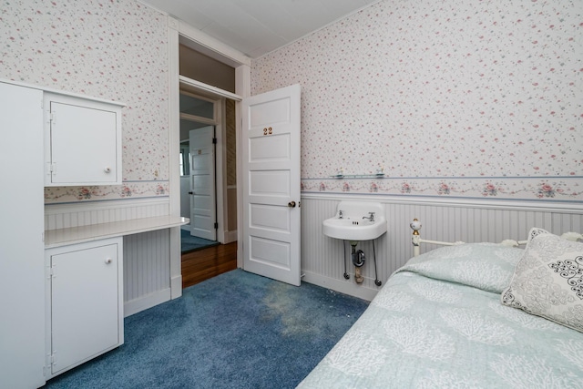 bedroom featuring dark colored carpet, wainscoting, and wallpapered walls