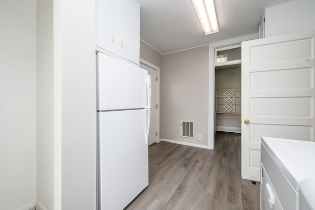 kitchen featuring freestanding refrigerator, washer / clothes dryer, light wood-style flooring, visible vents, and white cabinetry