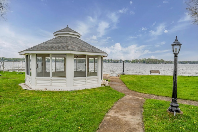 exterior space with a water view, a shingled roof, and a lawn