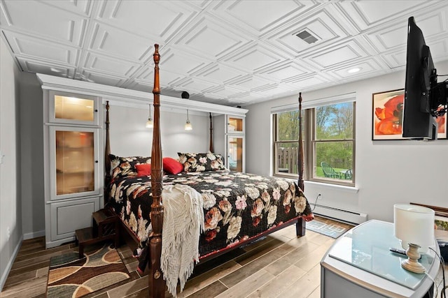bedroom with wood finished floors, baseboard heating, and an ornate ceiling