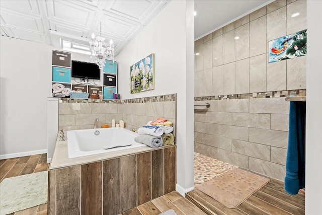 bathroom with wood finished floors, a notable chandelier, a bath, baseboards, and walk in shower