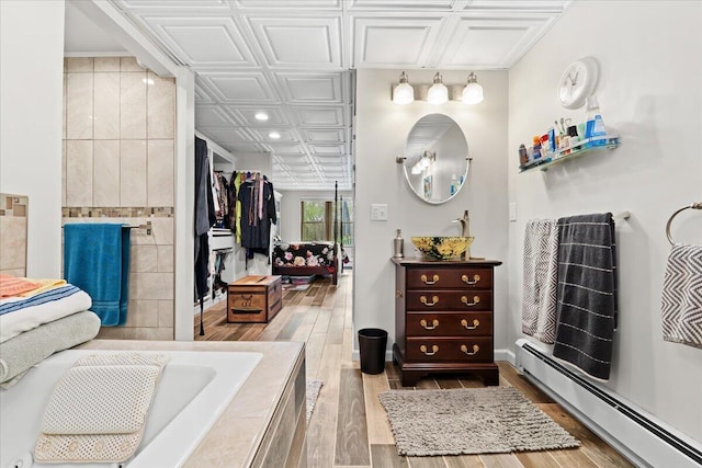 bathroom featuring an ornate ceiling, wood finished floors, a baseboard heating unit, vanity, and tiled tub