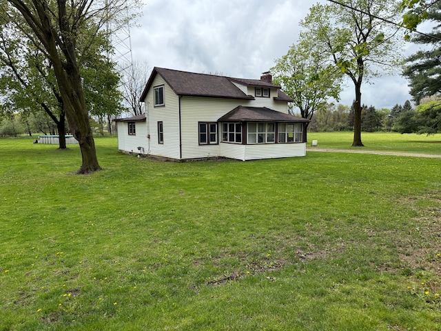 back of property featuring a chimney, roof with shingles, a yard, and a sunroom