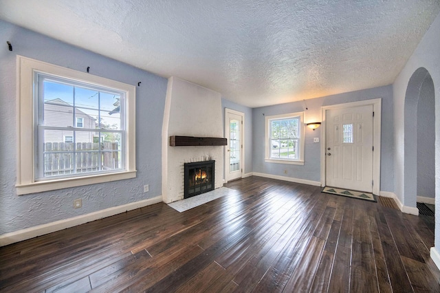 1009 S Webster St, Jackson, MI 49203 - unfurnished living room with a textured ceiling, dark wood-style flooring, baseboards, a fireplace, and arched walkways