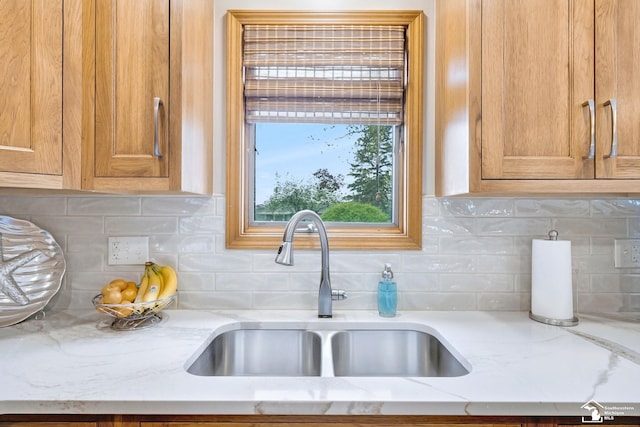 kitchen featuring backsplash, light stone countertops, and a sink