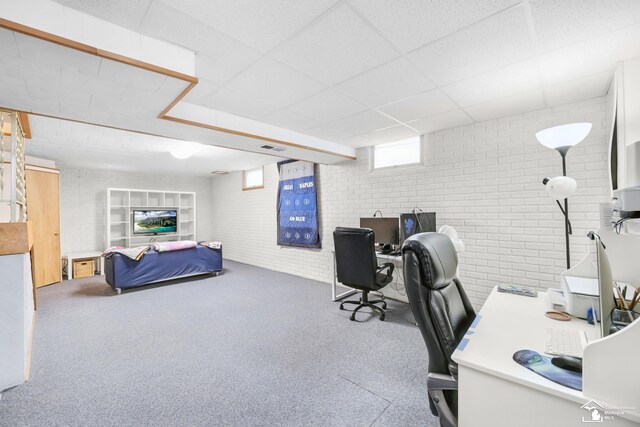 carpeted home office featuring brick wall and a drop ceiling