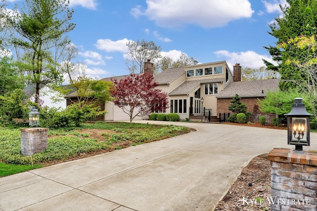 view of front of property featuring concrete driveway, a garage, a chimney, and brick siding