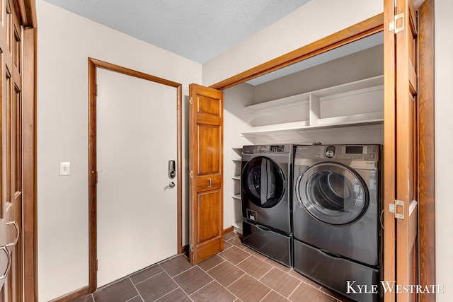 clothes washing area featuring washer and clothes dryer, laundry area, a textured ceiling, and dark tile patterned floors