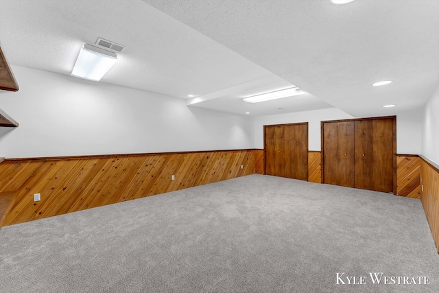 finished below grade area featuring wood walls, carpet flooring, a wainscoted wall, and visible vents