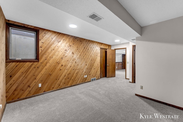 carpeted spare room with visible vents, wood walls, baseboards, and recessed lighting
